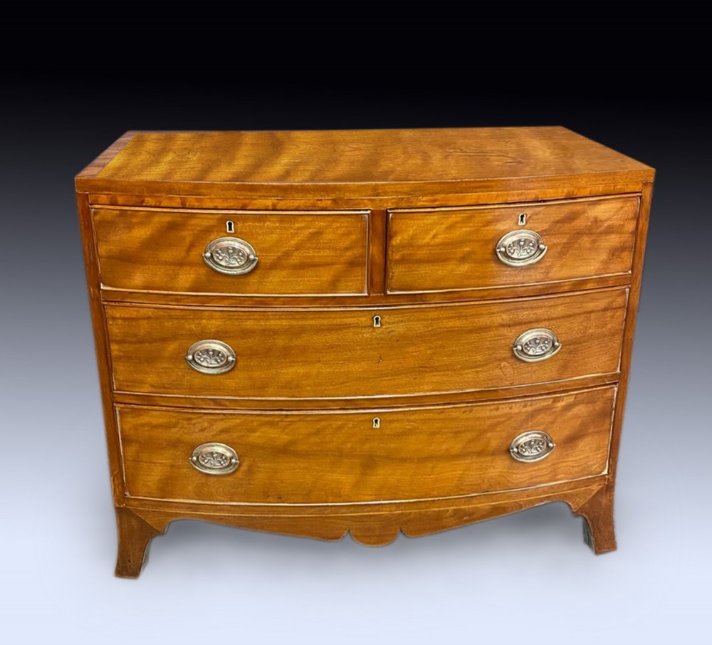 A George III bow-fronted satinwood chest of drawers with two short over two long drawers and oval brass handles. View II