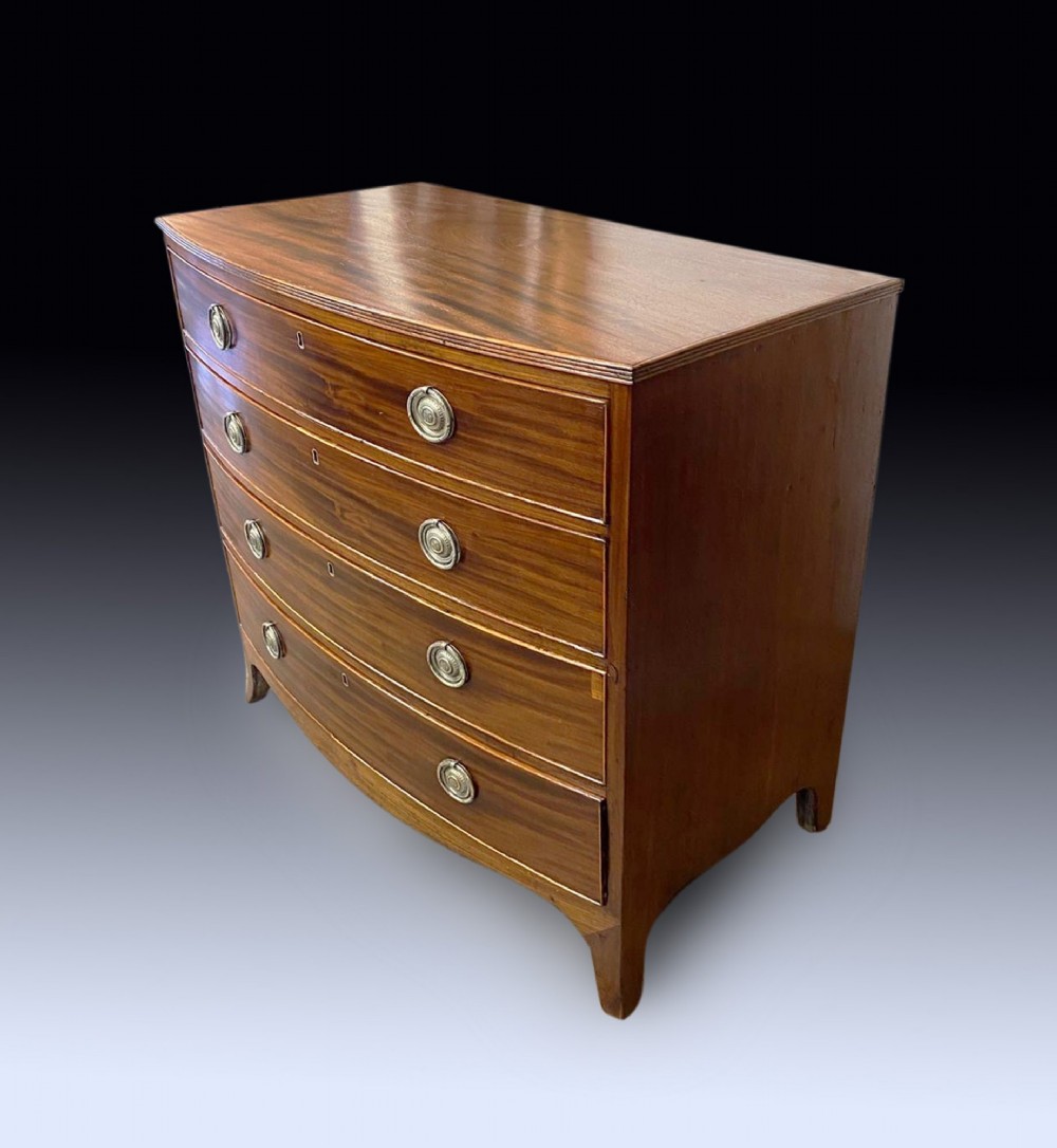 A George III mahogany chest of drawers featuring a curved bow front, four graduated drawers with circular brass ring handles, and short splayed feet. View II