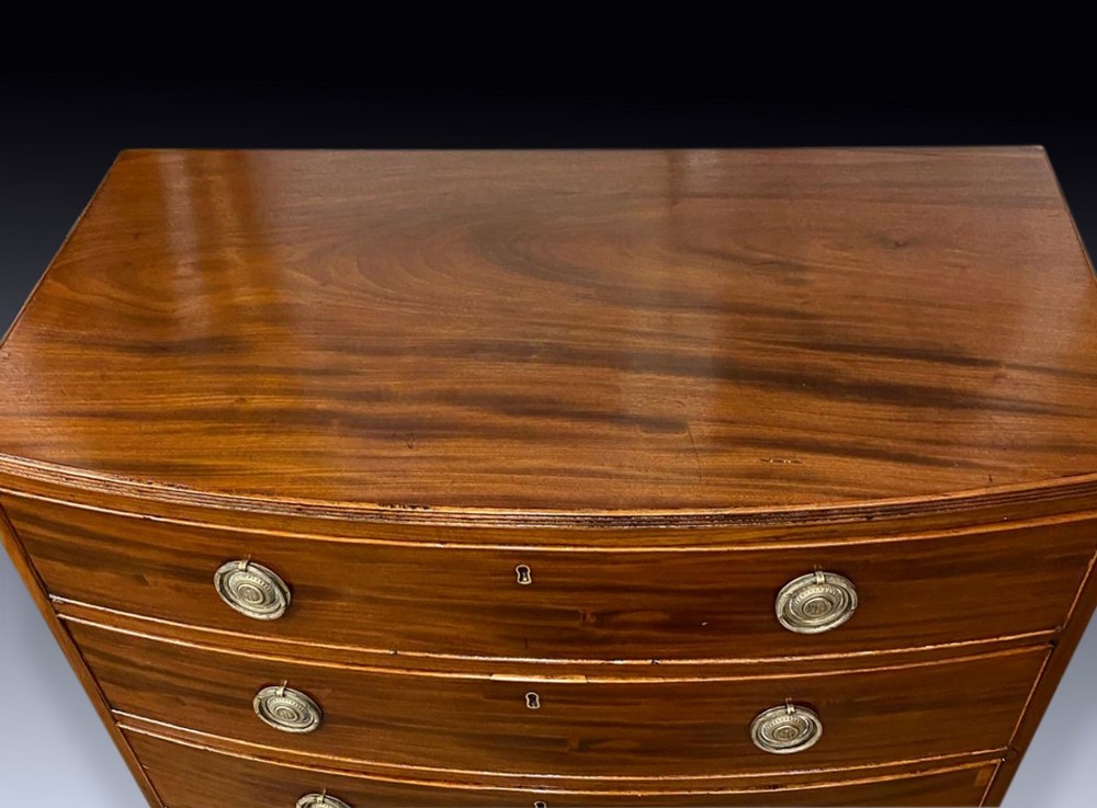 A George III mahogany chest of drawers featuring a curved bow front, four graduated drawers with circular brass ring handles, and short splayed feet. View III