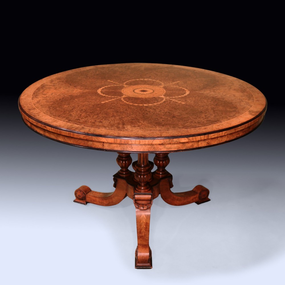 A circular mid 19th-century burr walnut centre table featuring central marquetry inlay and a carved pedestal base with splayed legs.