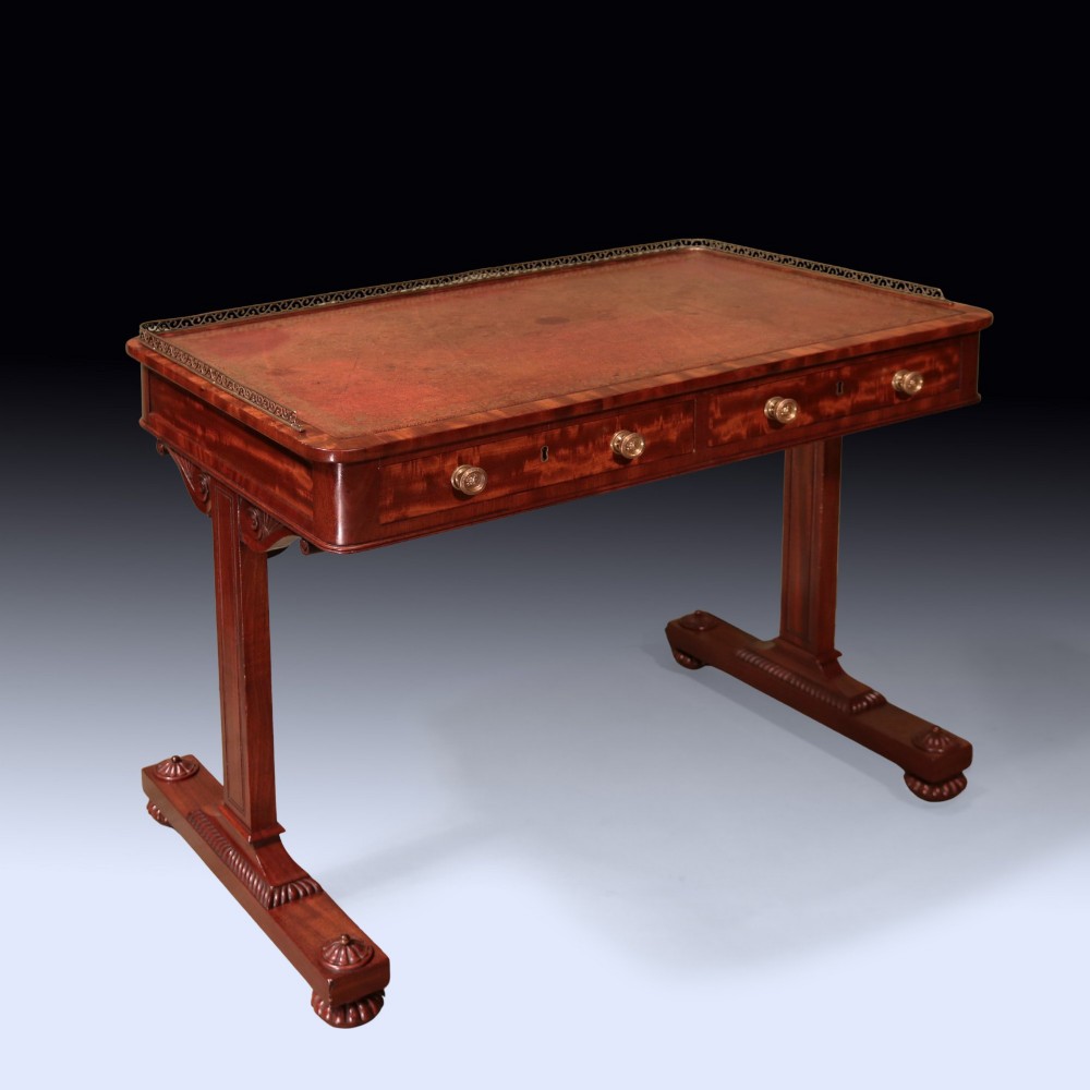An antique Regency period mahogany writing table featuring an inset leather top, a brass gallery rail, and drawers set on twin end supports.