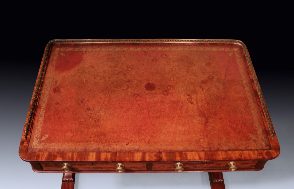 An antique Regency period mahogany writing table featuring an inset leather top, a brass gallery rail, and drawers set on twin end supports. View III