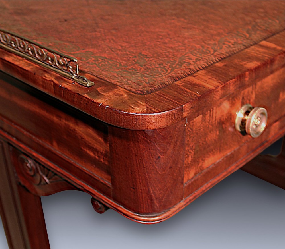 An antique Regency period mahogany writing table featuring an inset leather top, a brass gallery rail, and drawers set on twin end supports. View IV