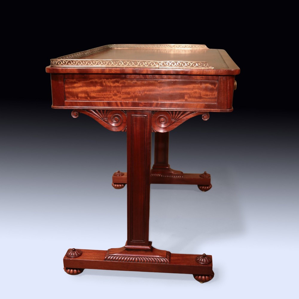 An antique Regency period mahogany writing table featuring an inset leather top, a brass gallery rail, and drawers set on twin end supports. View V