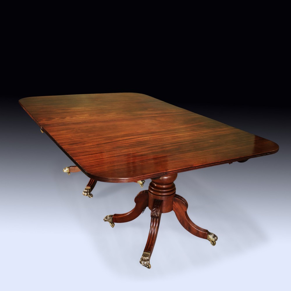 An early 19th-century mahogany twin pedestal dining table featuring rounded ends, turned central columns, reeded splayed legs, and brass claw castors.