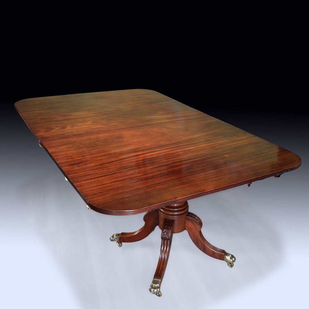 An early 19th-century mahogany twin pedestal dining table featuring rounded ends, turned central columns, reeded splayed legs, and brass claw castors. View II