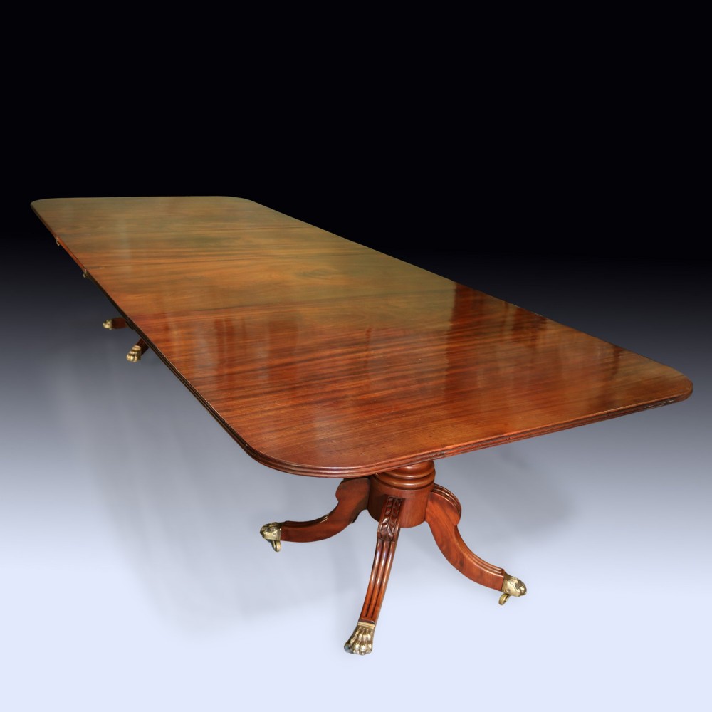 An early 19th-century mahogany twin pedestal dining table featuring rounded ends, turned central columns, reeded splayed legs, and brass claw castors. View IV