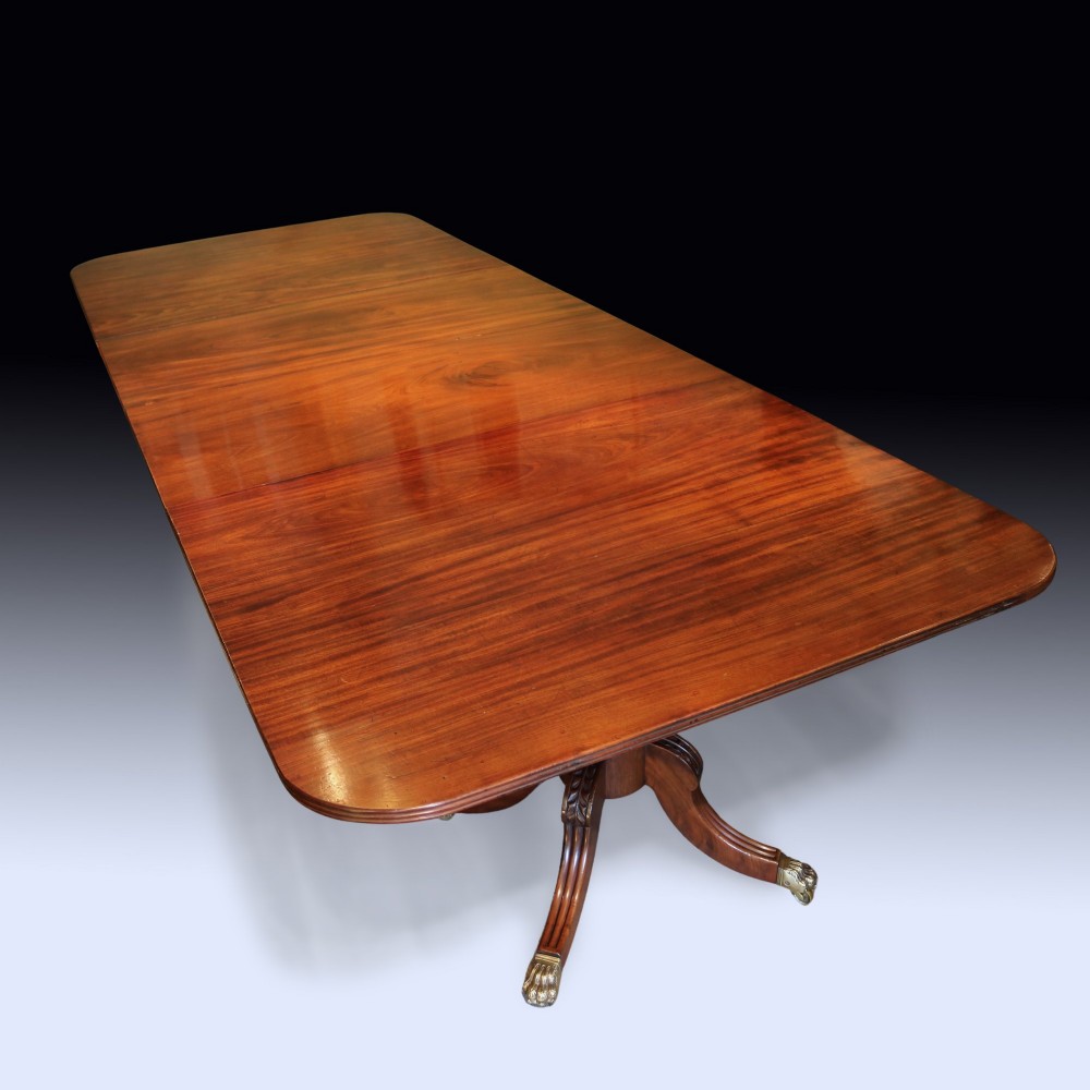 An early 19th-century mahogany twin pedestal dining table featuring rounded ends, turned central columns, reeded splayed legs, and brass claw castors. View V
