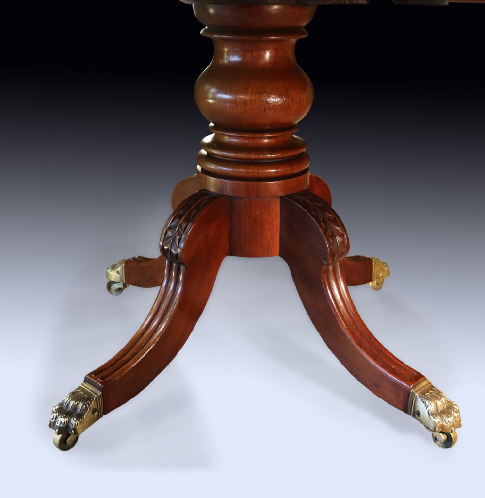 An early 19th-century mahogany twin pedestal dining table featuring rounded ends, turned central columns, reeded splayed legs, and brass claw castors. View VII