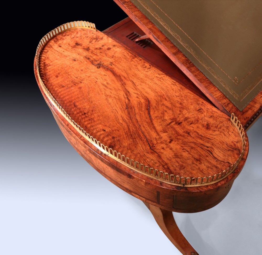 An early 19th century Regency burr oak writing table featuring a green leather inset top, brass gallery rails on raised side platforms, and trestle legs with brass castors. View III