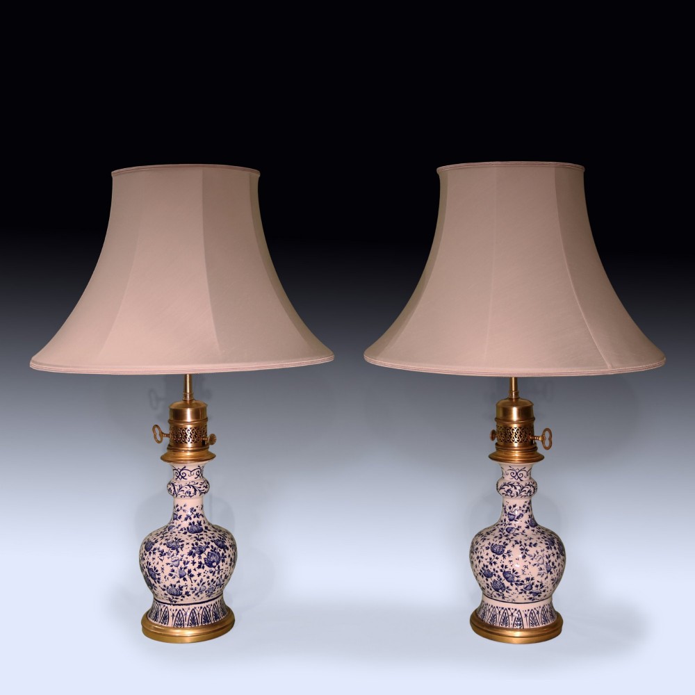 A pair of mid 19th century Chinese blue and white porcelain oil lamps with brass mounts and cream fabric shades.