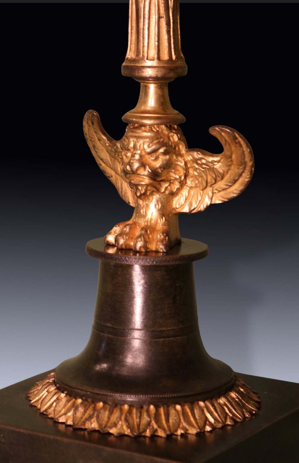 A pair of 19th-century French Empire style candlesticks featuring patinated bronze columns supported by gilded ormolu winged lions on square bases. View III