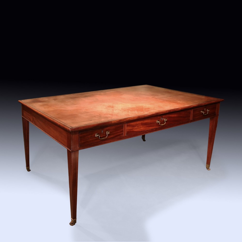 An antique George III mahogany writing table featuring an inset leather top, three frieze drawers with brass handles, and slender square tapered legs on castors. View II