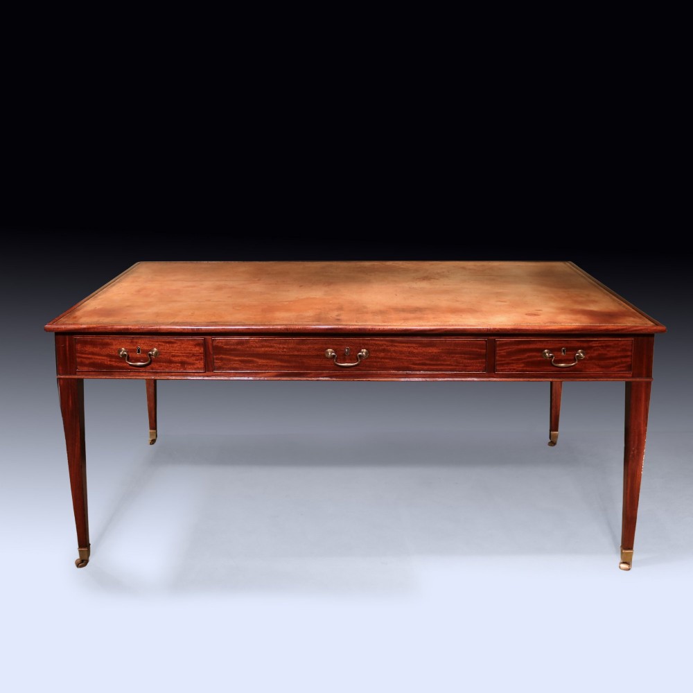 An antique George III mahogany writing table featuring an inset leather top, three frieze drawers with brass handles, and slender square tapered legs on castors. View III