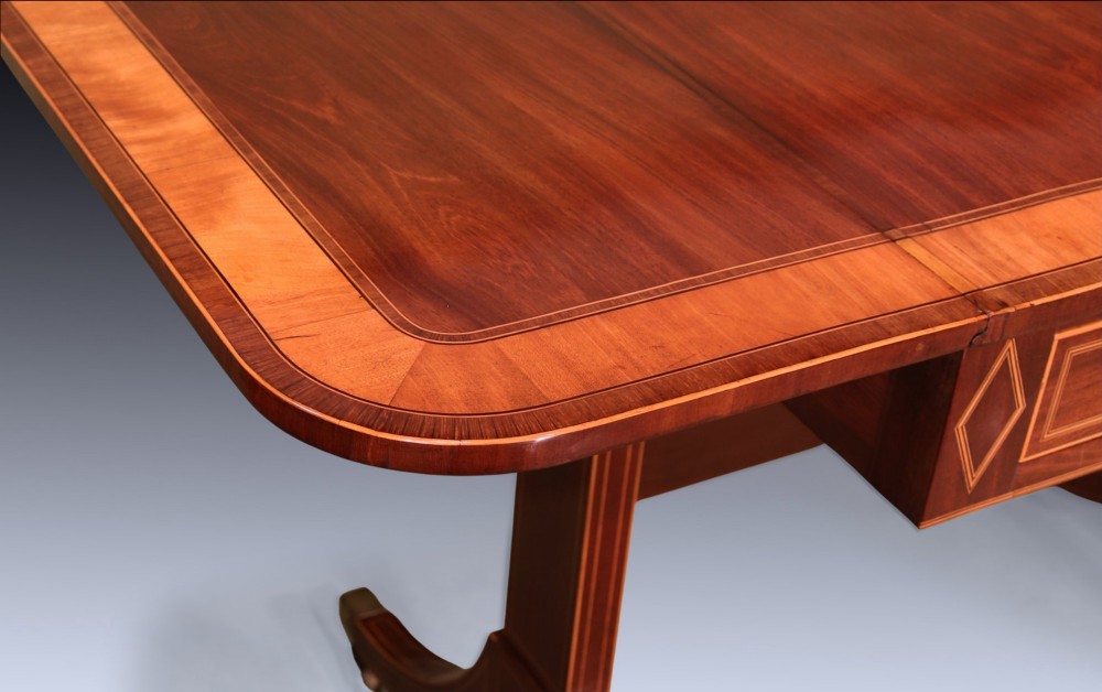 A George III mahogany sofa table featuring satinwood crossbanding, drop-leaf ends, two frieze drawers, and splayed legs on brass castors. View V