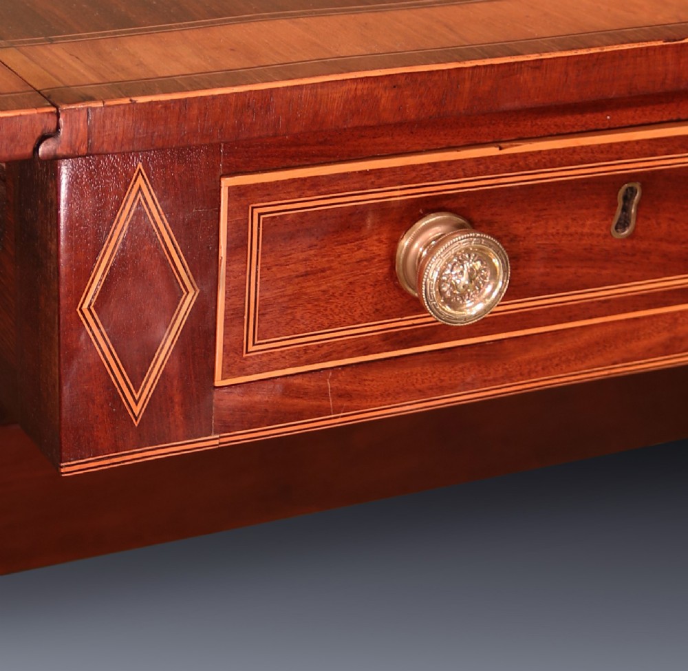 A George III mahogany sofa table featuring satinwood crossbanding, drop-leaf ends, two frieze drawers, and splayed legs on brass castors. View VI
