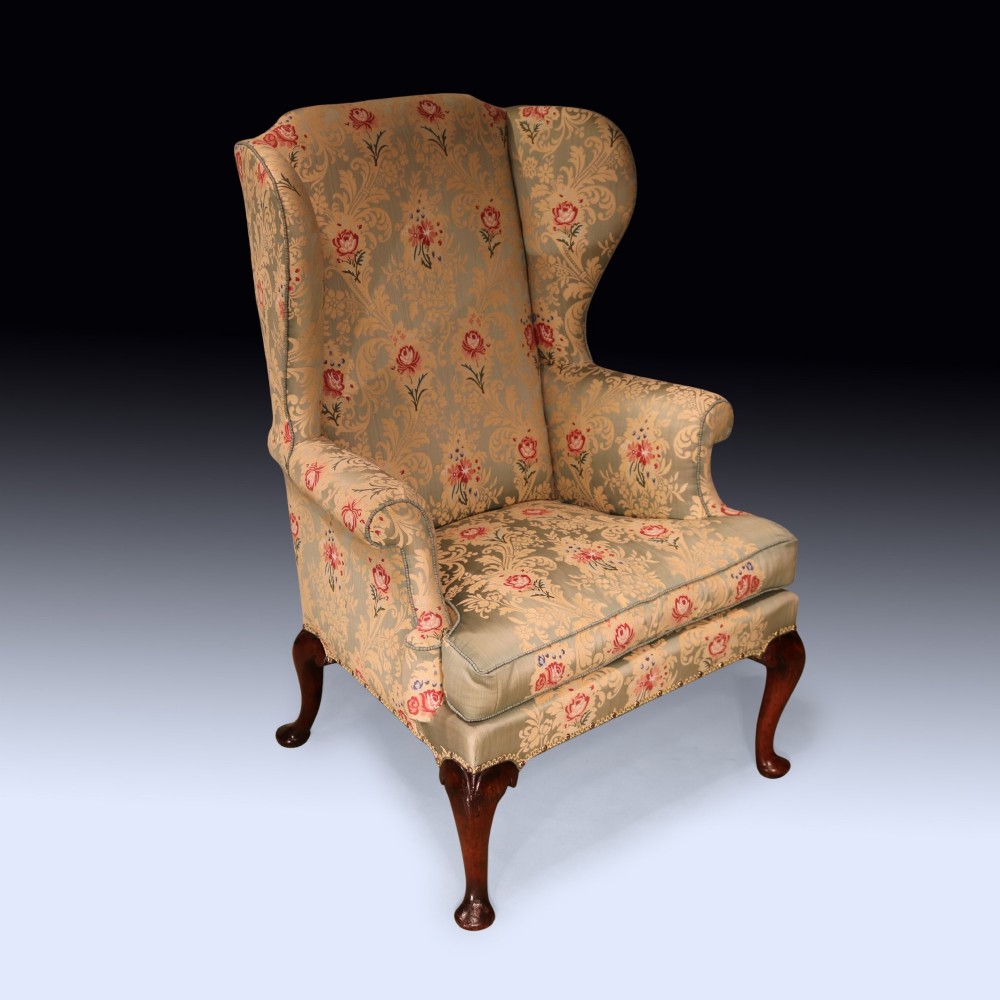 An early 18th-century wing armchair upholstered in patterned green and beige damask fabric with carved walnut cabriole legs. View II