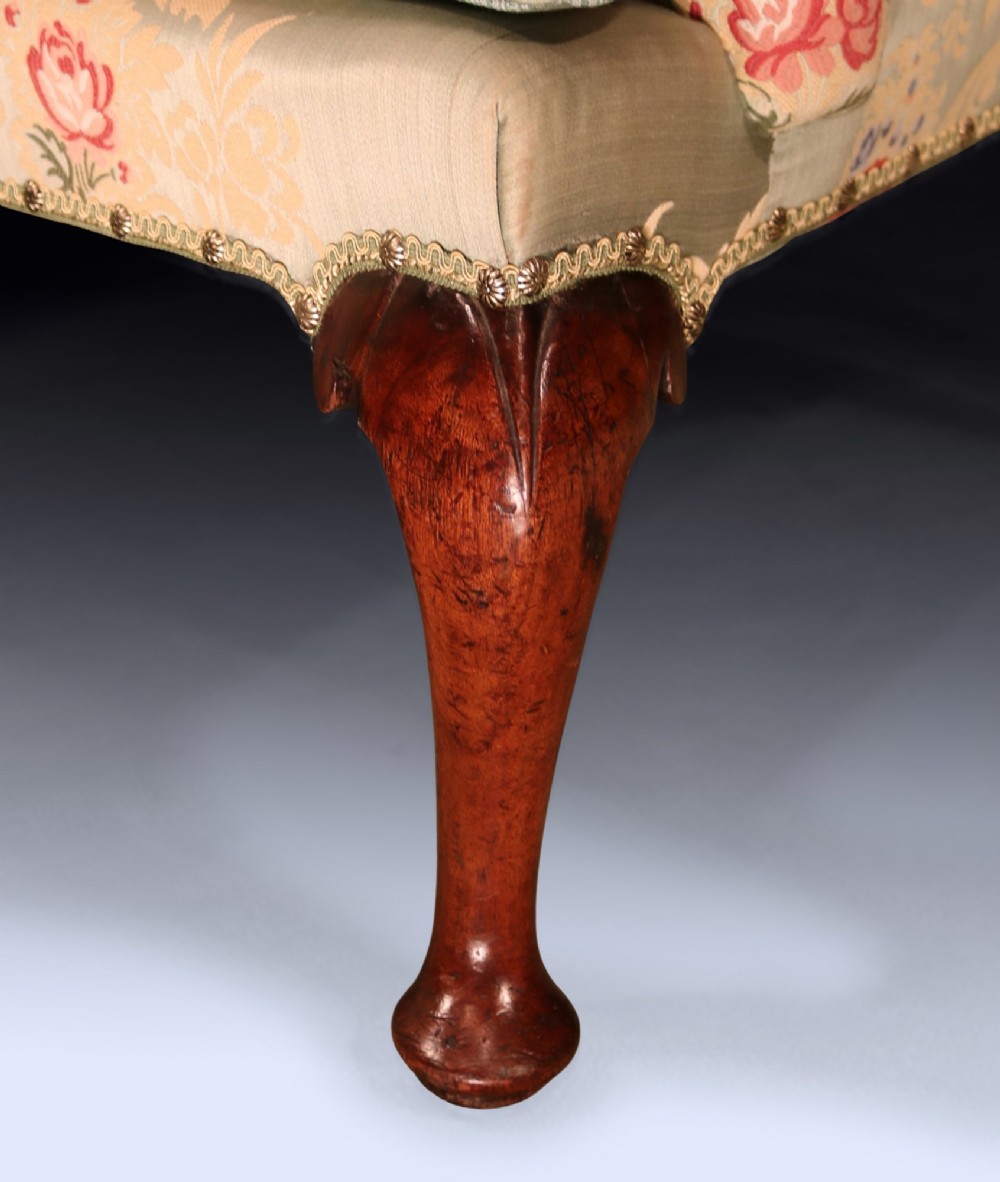 An early 18th-century wing armchair upholstered in patterned green and beige damask fabric with carved walnut cabriole legs. View IV