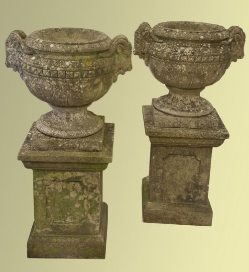 A Good Pair of Cast Stone Urns on Plinths with Goat Mask Handles and Lotus Leaves