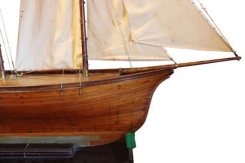 fig 1. A late nineteenth-century scratch-built wooden pond yacht featuring a carvel hull, ketch rigging, off-white canvas sails, and a fitted wooden display base.