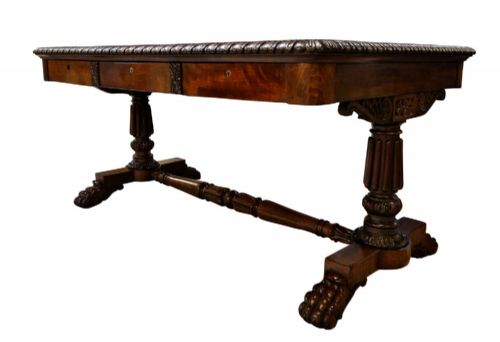 fig 3. A George IV mahogany partners writing table featuring a patterned top edge, three frieze drawers, carved pedestal supports, a turned stretcher, and claw feet.