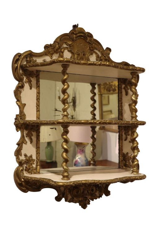 A French Rococo Revival painted and gilt wall etagere featuring three shelves, carved scrollwork, spiral columns, and a mirrored back.