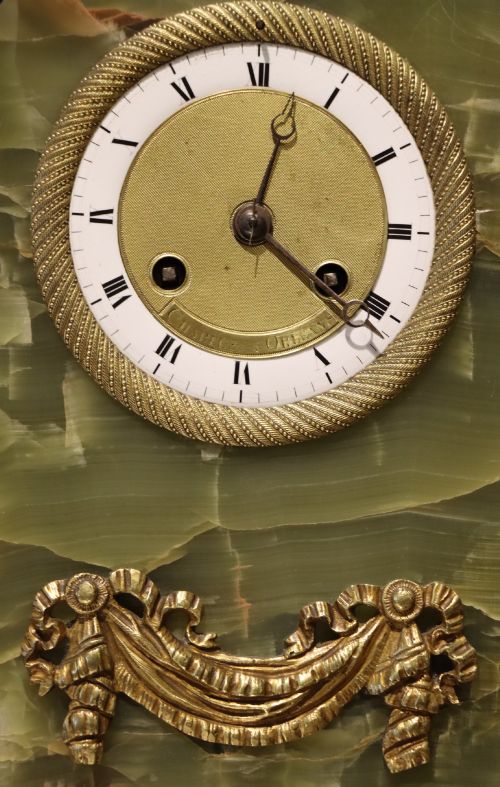 fig 2. An early nineteenth-century French mantel clock constructed from polished green onyx with an arched case, gilt-bronze ribbon swag mount, and a central dial with Roman numerals.