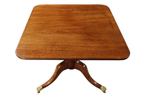 fig 2. A George III mahogany pedestal supper table featuring a rounded square tilt top, turned central column, and splayed legs with brass paw castors.