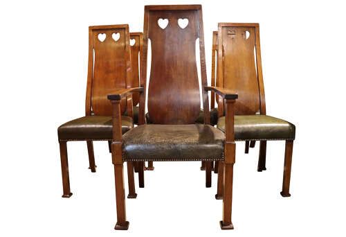 fig 1. A set of six Arts and Crafts solid oak dining chairs featuring tall backsplats with heart-shaped cutouts and green leather seats with brass studding.