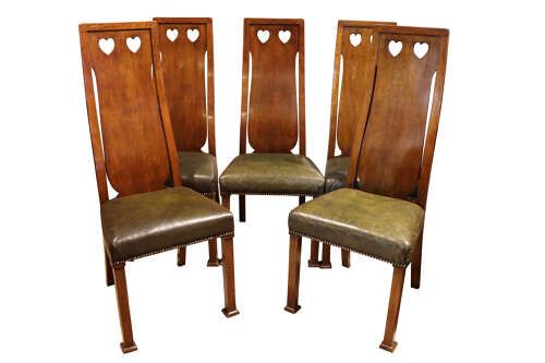 fig 2. A set of six Arts and Crafts solid oak dining chairs featuring tall backsplats with heart-shaped cutouts and green leather seats with brass studding.