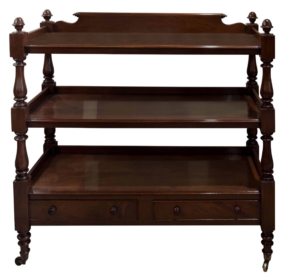 A nineteenth-century dark mahogany three-tier dumb waiter featuring turned support columns, two lower drawers, urn finials, and brass castors. View II