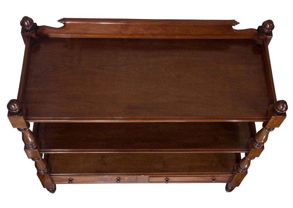 A nineteenth-century dark mahogany three-tier dumb waiter featuring turned support columns, two lower drawers, urn finials, and brass castors. View V