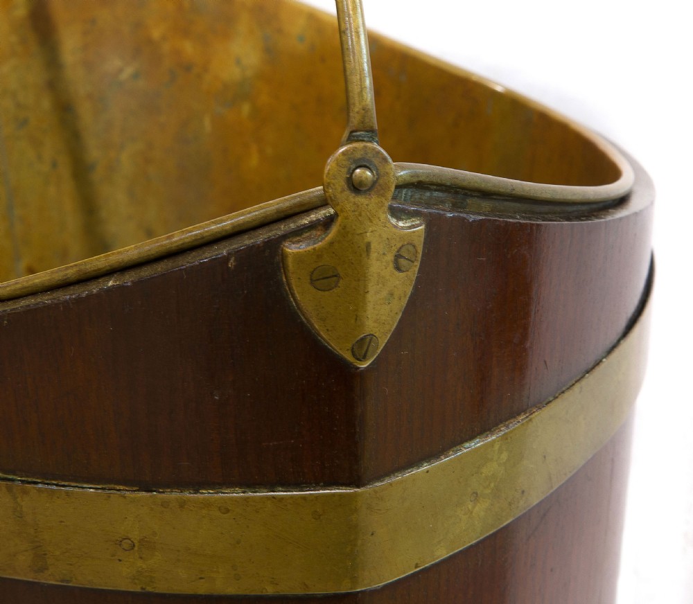 A late Georgian coopered mahogany bucket featuring brass horizontal banding, a removable inner brass liner, and a brass swing handle. View V