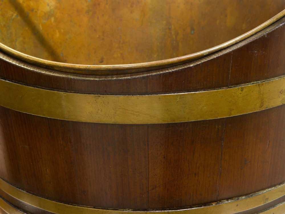A late Georgian coopered mahogany bucket featuring brass horizontal banding, a removable inner brass liner, and a brass swing handle. View VI