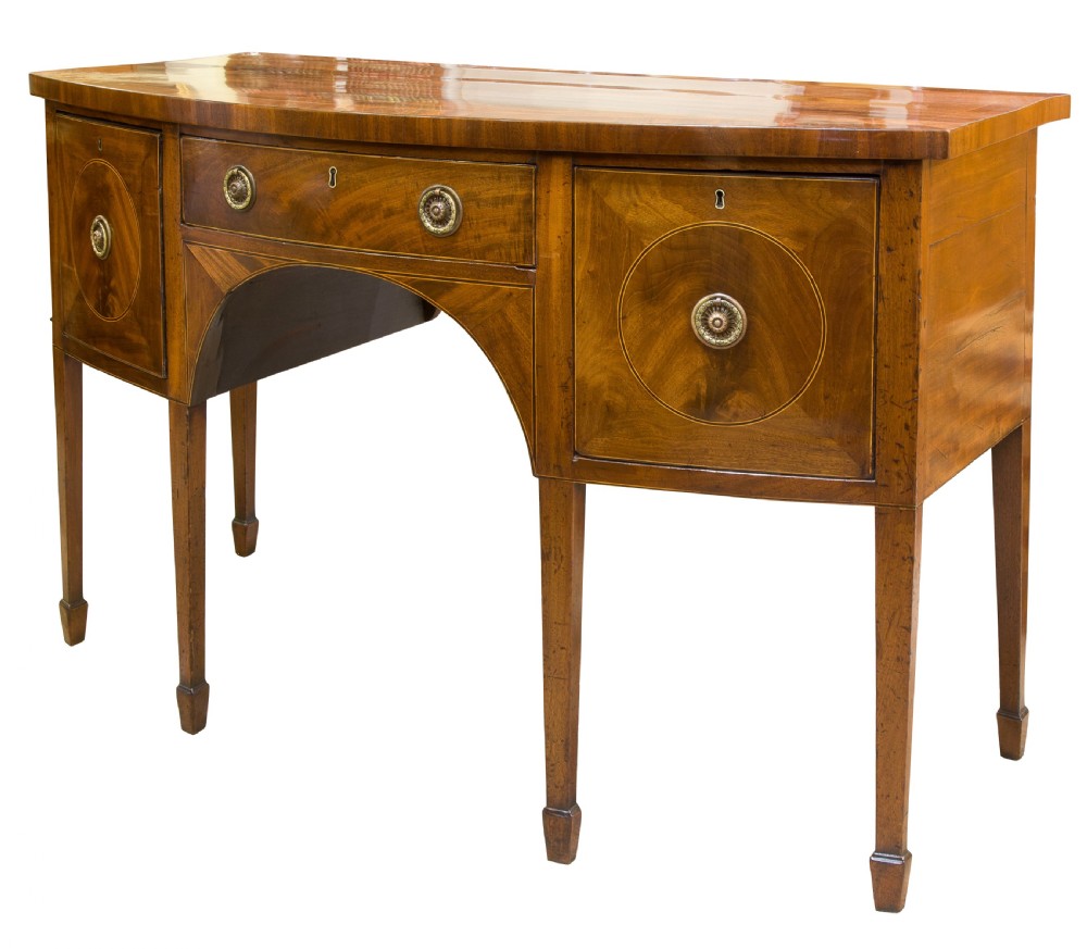A George III mahogany bowfront sideboard featuring inlaid circular cupboard doors, a central drawer, and square tapered legs terminating in spade feet.