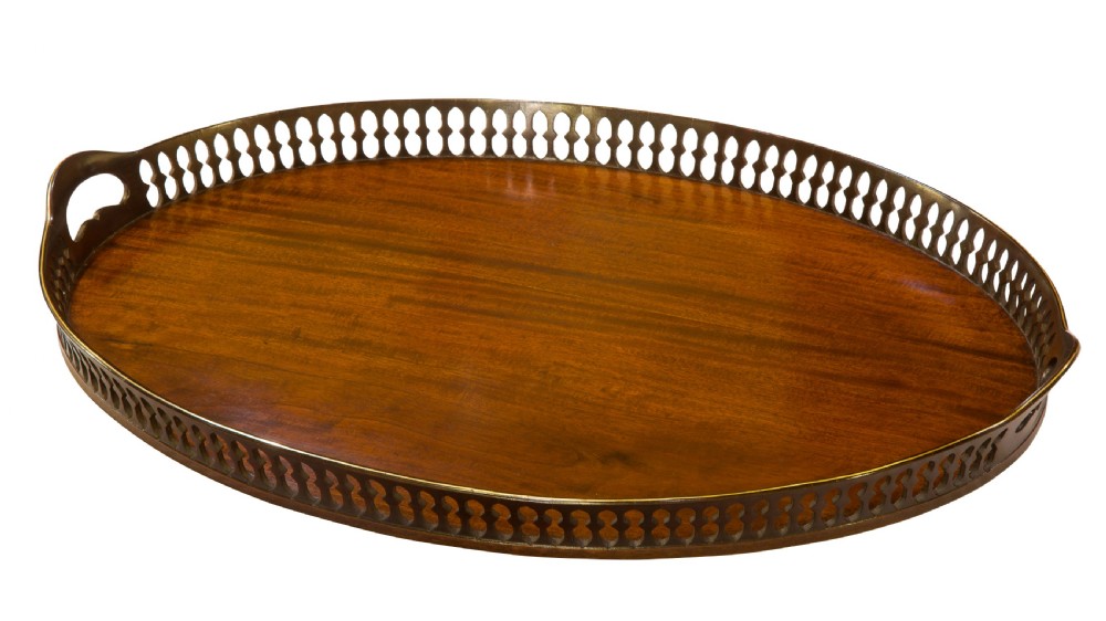 An oval mahogany serving tray with a polished dark wood grain and a raised pierced brass gallery featuring open handle grips.