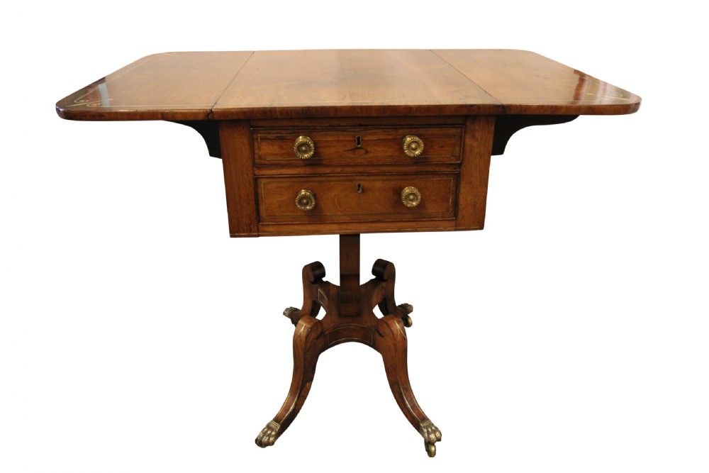 A Regency period rosewood drop-leaf work table featuring two drawers with circular brass knobs, supported by a central pedestal and four curved legs with brass lion paw castors.