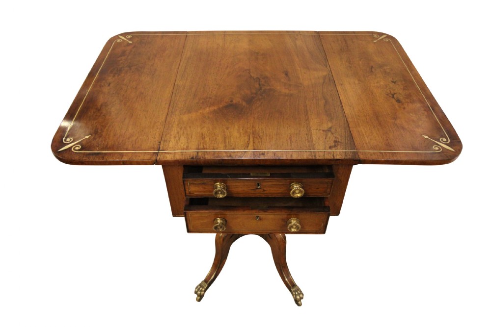 A Regency period rosewood drop-leaf work table featuring two drawers with circular brass knobs, supported by a central pedestal and four curved legs with brass lion paw castors. View II