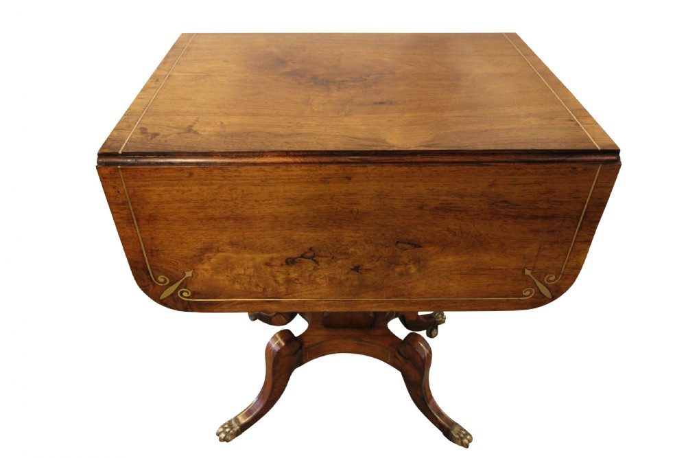 A Regency period rosewood drop-leaf work table featuring two drawers with circular brass knobs, supported by a central pedestal and four curved legs with brass lion paw castors. View VI