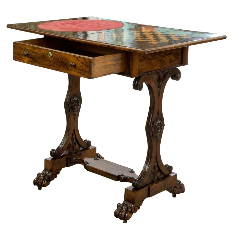 An antique Regency period dark rosewood games table featuring a rectangular fold-over top, frieze drawer with brass escutcheon, carved trestle supports, and claw feet with brass castors. View II