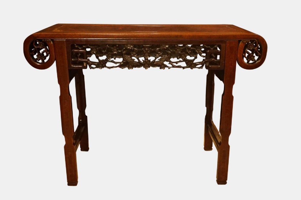 A dark hardwood Chinese altar table featuring everted scroll ends, raised straight legs, and an intricately carved openwork apron.