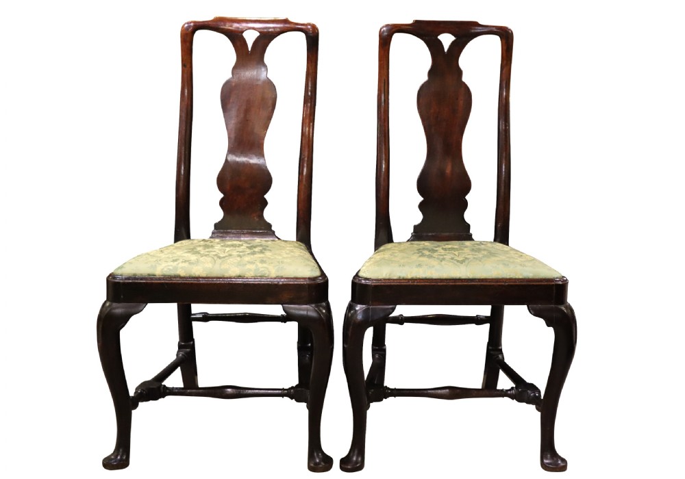 A pair of George I style walnut side chairs featuring high carved backrests with vase splats, cabriole front legs, and green pattern upholstered seats.