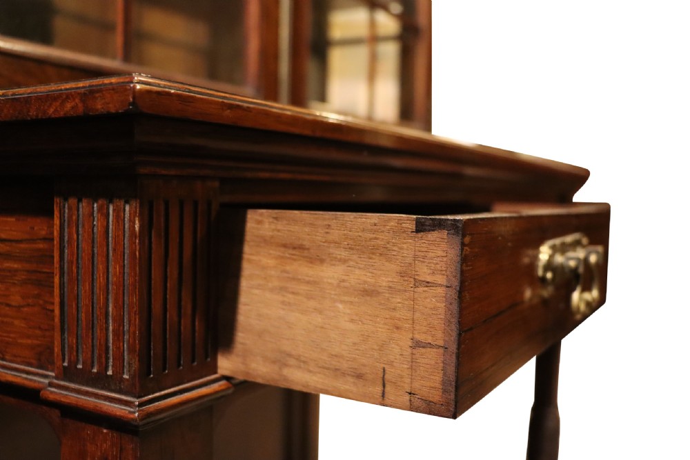 An antique rosewood cabinet on stand featuring glazed double doors, brass corner mounts, two frieze drawers, and an open lower shelf. View IV