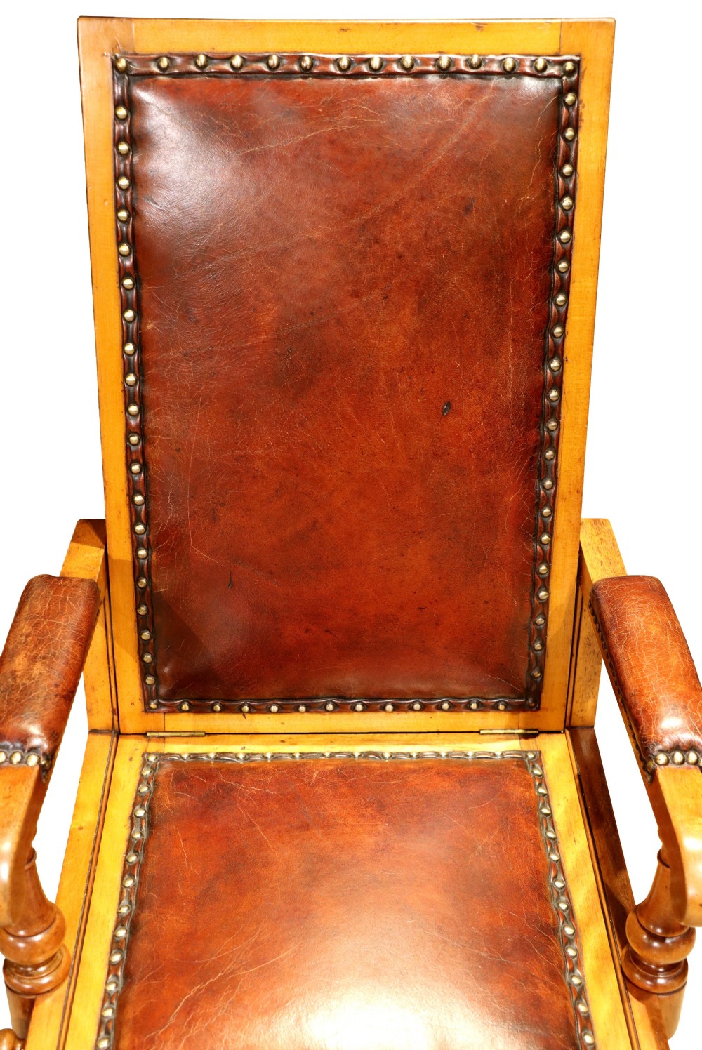 A Victorian childs reclining chair crafted from light timber with studded warm brown leather upholstery, turned arm supports, and brass castors. View III