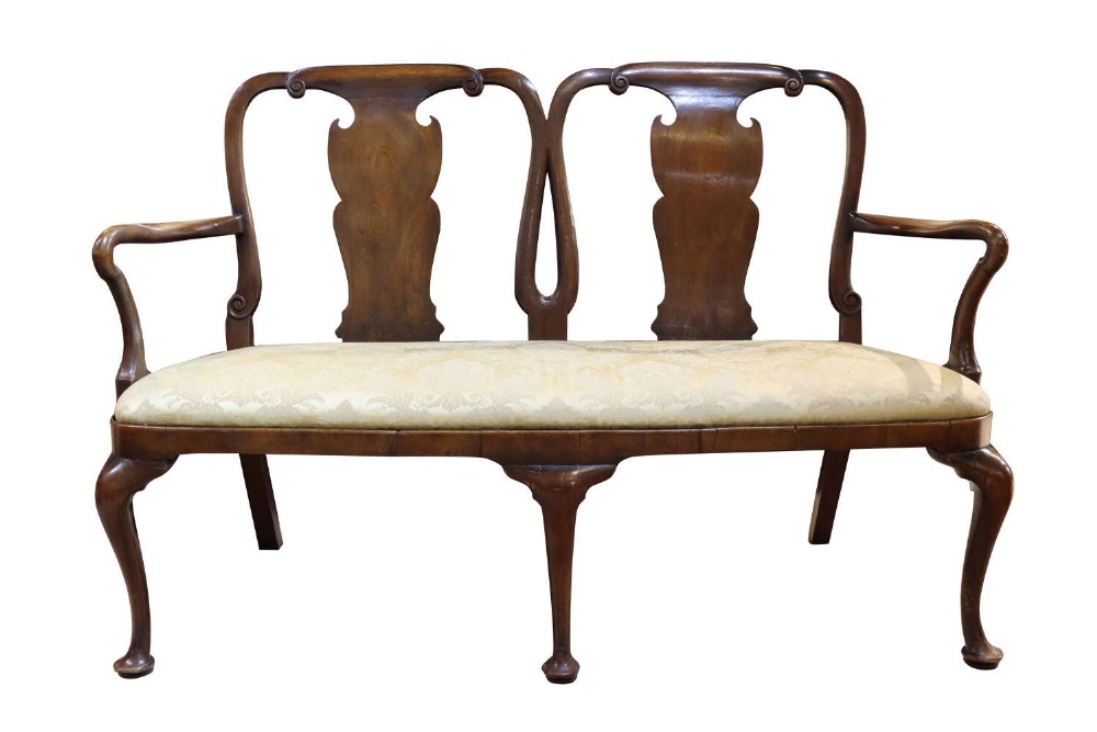 A George II style oak double chairback settee featuring two shaped splats, swept armrests, cabriole front legs with pad feet, and a cream fabric seat.