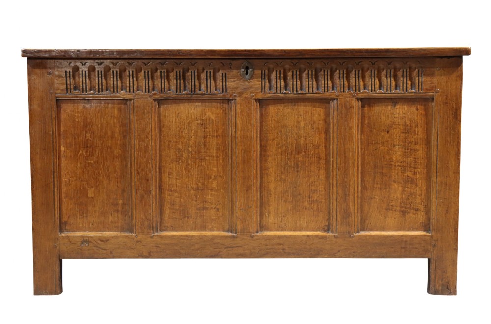 An 18th-century oak panelled coffer featuring four recessed front panels, carved frieze detailing along the top rail, and a central brass escutcheon.