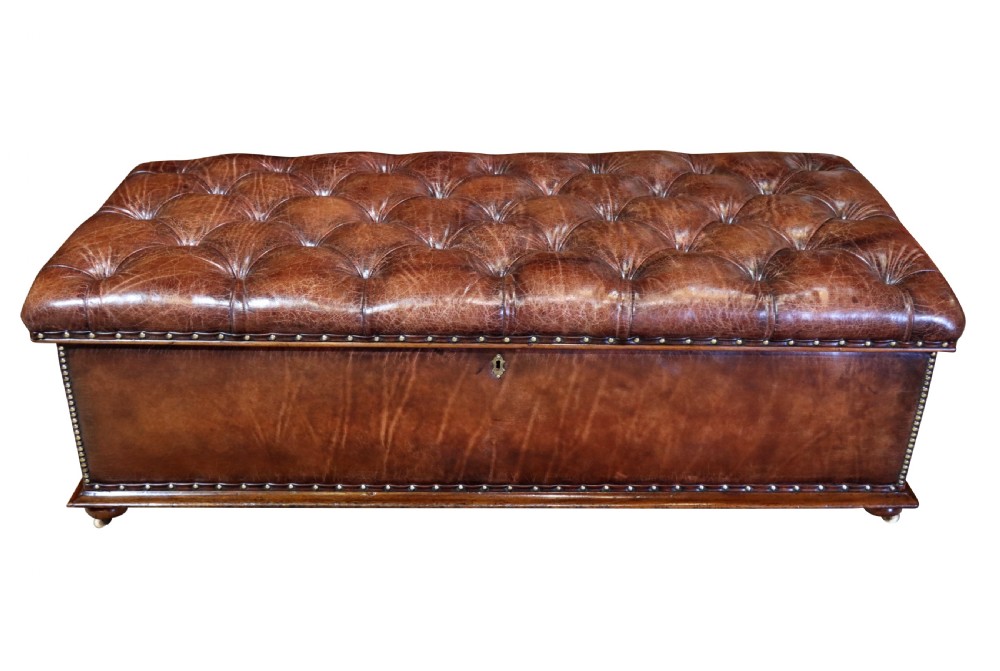 A large 19th-century rectangular leather ottoman with deep buttoned upholstery, brass stud trim, and short wooden feet on castors.