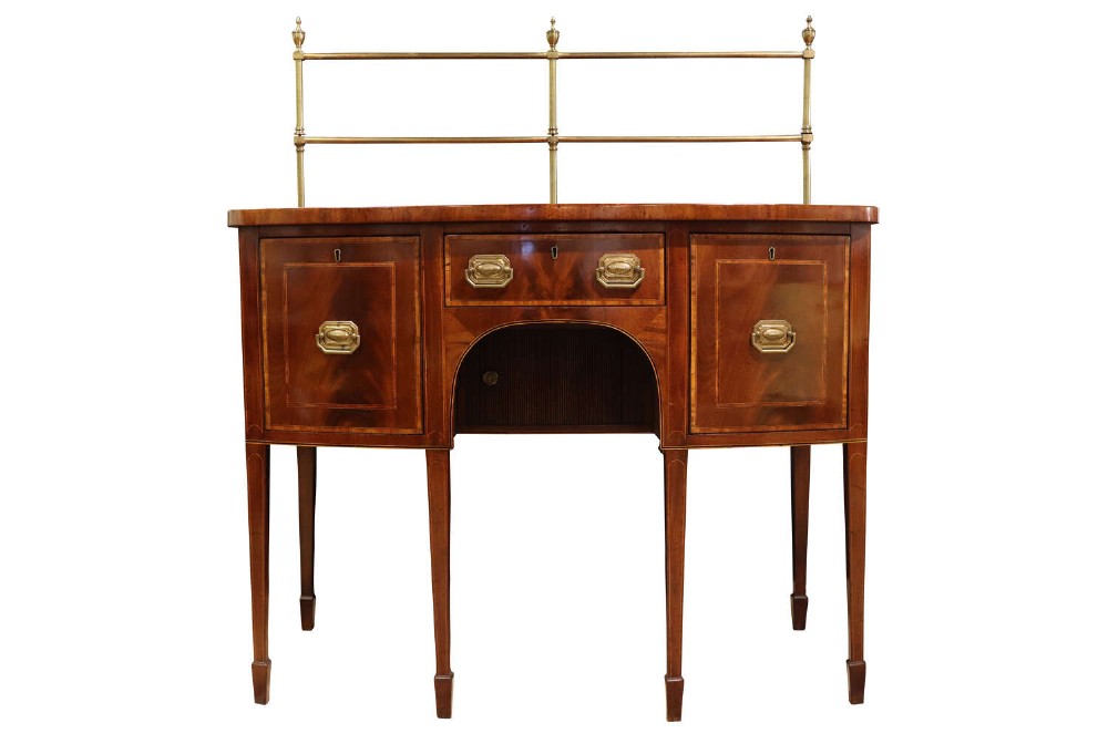 An 18th-century Georgian Sheraton bowfront mahogany sideboard featuring a brass gallery, inlaid drawers, and slender square tapered legs with spade feet.