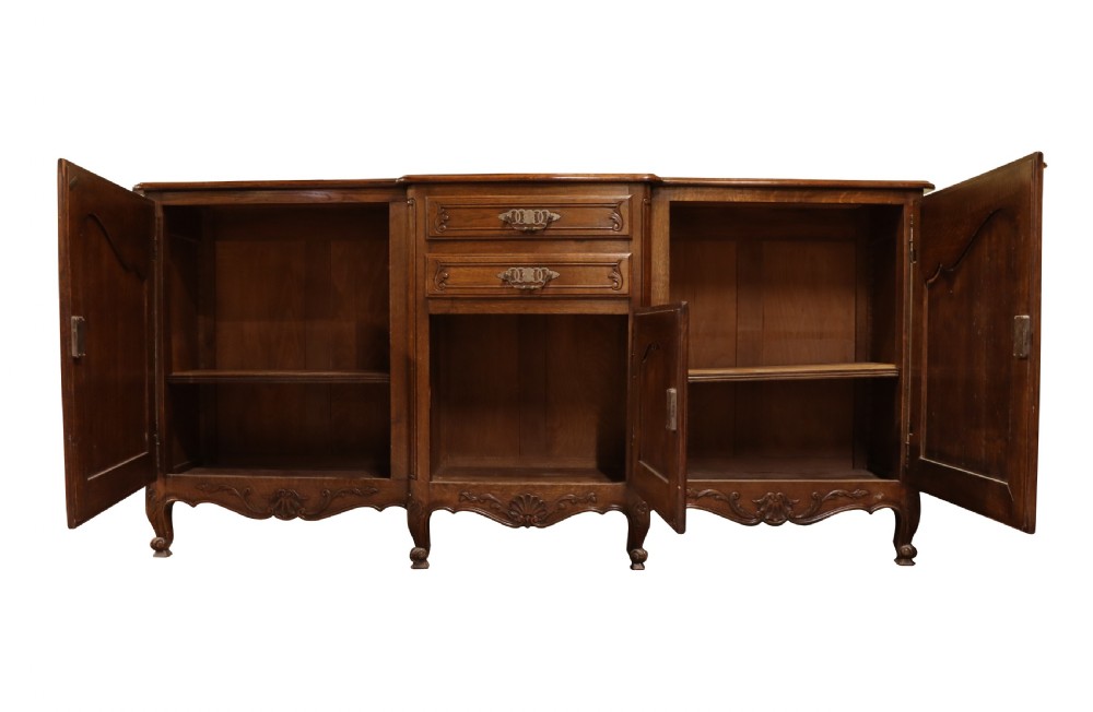 A French Louis XV style warm brown oak sideboard featuring three carved panel doors, two central drawers, brass hardware, and cabriole feet. View II
