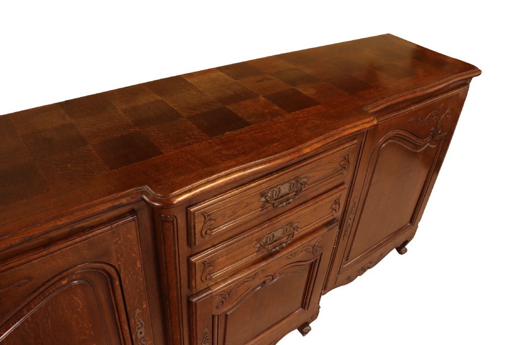 A French Louis XV style warm brown oak sideboard featuring three carved panel doors, two central drawers, brass hardware, and cabriole feet. View III